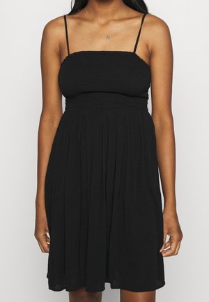 Robe noire sans manches avec un corsage froncé, jupe fluide et fines bretelles réglables. Tissu doux et léger avec une texture plissée.