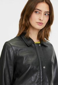 Schwarze Lederjacke mit strukturiertem Kragen und Druckknöpfen, mit glatter Textur und minimalistischem Design.
