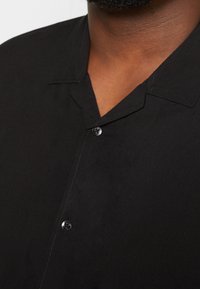 Zwarte blouse met een gestructureerde stof, met een V-hals en een knoopsluiting aan de voorkant. Elegante, minimalistische uitstraling.