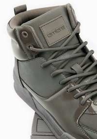 Bota alta en cuero gris oscuro y material sintético. Cuenta con acentos texturizados, diseño con cordones y un collar acolchado para mayor comodidad.