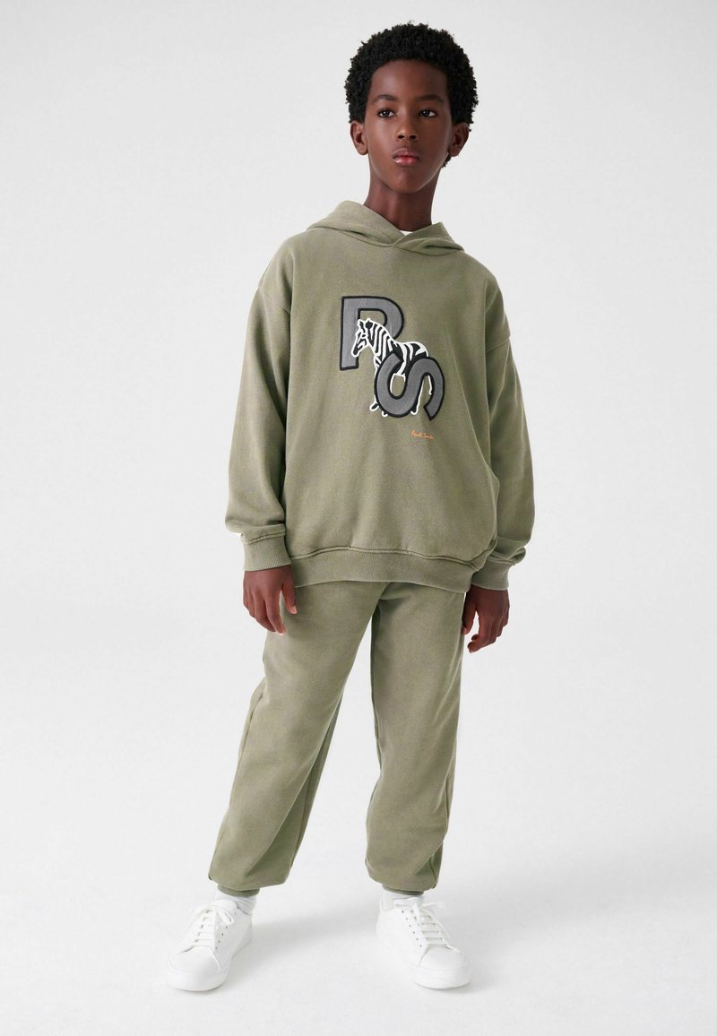 Oliven grøn hættetrøje med zebra-grafik og 'PS'-logo, parret med matchende sweatpants. Har en afslappet pasform og er fremstillet af tekstureret stof. Hvide sneakers.