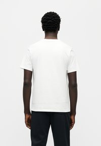 Λευκό βαμβακερό T-shirt με κοντά μανίκια και στρογγυλή λαιμόκοψη, εμφανιζόμενο από πίσω. Απλός σχεδιασμός, λεία υφή, άνετη εφαρμογή.