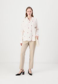 Button-up white blouse with red embroidery, paired with beige tailored pants and black patent leather heeled shoes, complemented by a cream bag.