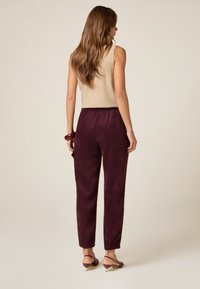 Beige mouwloos topje en bordeauxkleurige corduroy broek met elastische tailleband. Geweven stof met taps toelopende pijpen en aansluitende boorden.