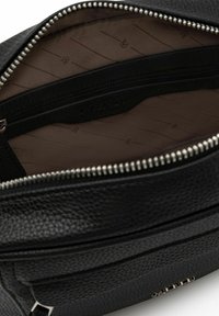 Zwarte leren tas met textuur en een ritsluiting. Het interieur heeft een gladde bruine voering en een subtiele logo-opdruk. Inclusief externe ritszak.