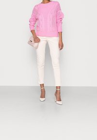 Pink knitted sweater with textured patterns, paired with white slim-fit pants and nude block-heeled shoes; holding a light pink handbag.