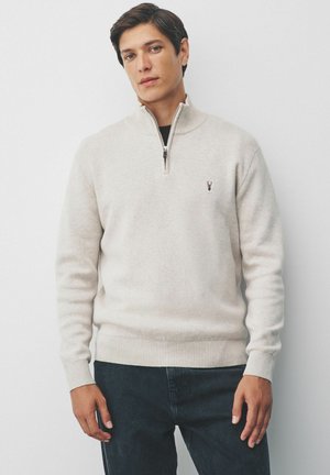 Suéter medio zip color beige claro, hecho de una tela suave, con puños y dobladillo acanalados, y un pequeño logo en el pecho.