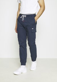 Tmavě modré kalhoty s pružným pasem na gumu a šňůrkou, postranní kapsy a nákladní kapsa. Zúžené nohavice s elastickými lemy. Vyrobené z lehké tkaniny.