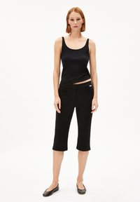 Zwart geribd tanktop gecombineerd met zwarte cropped broek met zijzakken. Het model staat op een witte achtergrond. Platte zwarte schoenen worden gedragen.