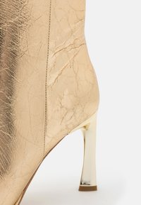 Gull høyhælte støvler med teksturert, krøllet lær overdel og blank, metallisk stiletthæl. Enkelt design med minimal detaljering.