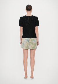 Top nera texturizzata con maniche a sbuffo, dotata di chiusura sul retro. Abbinato a pantaloni corti chiari con un motivo di palme nei toni del verde e del blu.