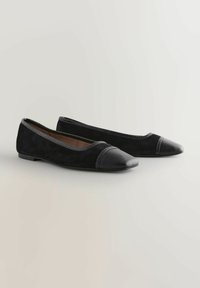 Ballerines en daim noir pour femmes avec bouts pointus en cuir noir et talons plats bas sur un fond neutre.