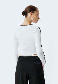 Witte geribde longsleeve top met zwarte afwerking, gecombineerd met zwarte broeken. De top heeft een cropped ontwerp en een ronde hals.