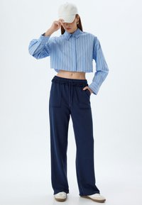 Geknipte, blauw gestreepte blouse met lange mouwen, gecombineerd met marineblauwe wijde broek met een elastische tailleband en zijzakken.