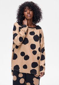 Długi top z długim rękawem w duże czarne kropki, o luźnym kroju i okrągłym dekolcie. Miękka tkanina o lekko teksturowanym wyglądzie.