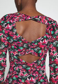 Robe fleurie à manches longues, avec un fond noir et un motif vibrant rose, vert et blanc. Détail découpé dans le dos.