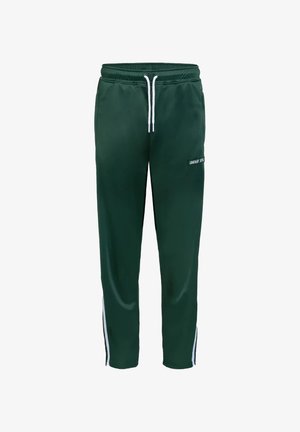 Pantalon de sport vert avec des bandes blanches sur les côtés et un cordon blanc, porté avec des baskets blanches et grises.
