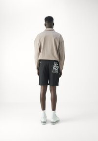 Camisa de manga larga beige, pantalones cortos negros con detalle de logo, zapatos deportivos y calcetines blancos. Diseño simple, ajuste relajado y texturas suaves.