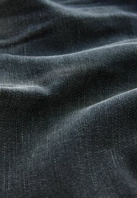Gros plan d’un tissu denim bleu foncé montrant la texture, le tissage diagonal et des plis doux créant des ombres et des reflets.