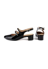 Escarpins en cuir verni noir avec bout carré, petit talon carré et deux ankle straps ajustables avec boucles en argent. Texture lisse, design minimaliste.