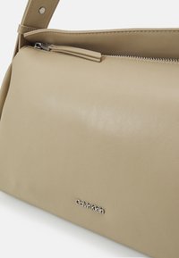 Borsa a spalla in pelle beige con zip superiore e logo Calvin Klein argentato sul davanti.