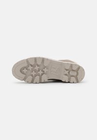 Suela de zapato con una superficie de goma texturizada, de color beige claro, con un patrón rugoso y un pequeño logo cerca del talón.