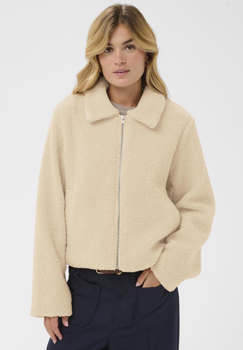 Beežist fliisist jope kraega kaelusega, esiküljel tõmblukuga ja laia lõikega varrukatega. Pehme tekstuur ja hubane välimus.