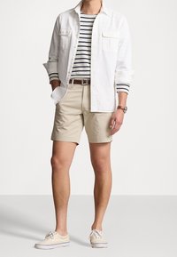 Bílá košile na knoflíky přes námořnickou a bílou pruhovanou triko, béžové šortky a světlé boty. Výrazné detaily: dvě náprsní kapsy a hnědý opasek.