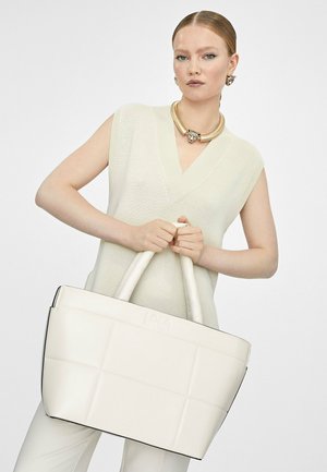 Bolso tote de cuero blanco con un diseño acolchado y ribetes negros, que cuenta con dos asas y un logo en relieve en la parte frontal.