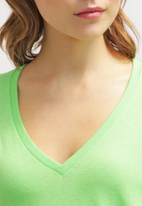 V-ringad t-shirt i ljusgrön bomull. Mjuk textur, figursydd form, med en ren halsringning och en svag lyster. Inga synliga mönster eller detaljer.