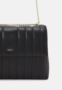 Czarna pikowana torebka z gładkiej skóry, z paskiem na łańcuszku w złotym odcieniu, płaskim prostokątnym kształtem i subtelnym logo z przodu.