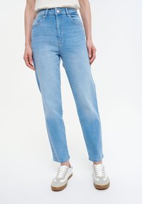 Jeans de tiro alto de color azul claro con un diseño de pierna recta, hechos de tela vaquera, con bolsillos visibles y un cierre de botón, combinados con zapatos en tonos neutros.