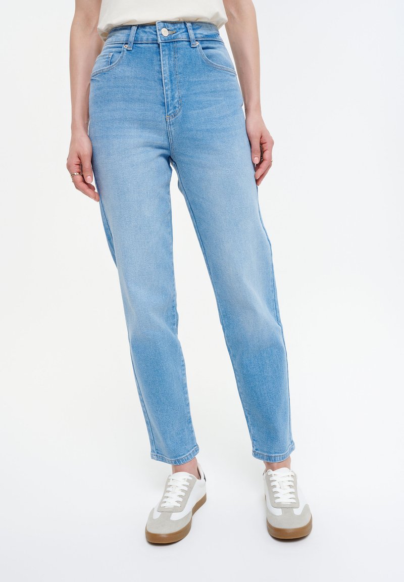 Jeans de tiro alto de color azul claro con un diseño de pierna recta, hechos de tela vaquera, con bolsillos visibles y un cierre de botón, combinados con zapatos en tonos neutros.