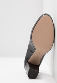 Escarpin en cuir noir avec un bout arrondi, une semelle texturée et une semelle intérieure beige. Le talon est modérément épais, offrant une bonne stabilité.