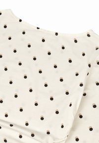 Korte mouwen, crèmekleurig topje van zachte stof met een patroon van kleine, effen zwarte, beige en lichtbruine stippen.