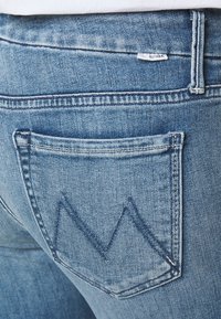 Vaaleansiniset farkut, joissa on hieman haalistunut pinta, takataskussa on siksak-ommeltu kuvio ja vyötäröllä pieni brändilogo.