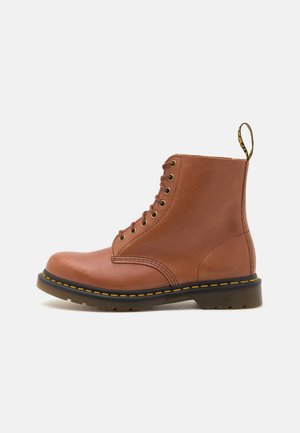 Botte homme en cuir marron à lacets avec semelle noire et couture jaune, avec une languette en boucle à l’arrière.