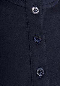 Marineblaue Poloshirt aus strukturiertem Stoff, mit drei schwarzen Knöpfen und Logo-Highlights am Kragen.