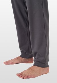 Graue Jogginghose mit elastischen Bündchen, aus einem weichen, dehnbaren Material. Barfuß zu sehen unter den Hosenbeinen.