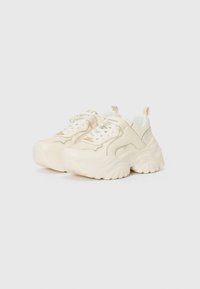 Chunky cream-colored sneakers with a textured sole, lace-up design, prominent stitching, and a tab at the heel for easy wear.