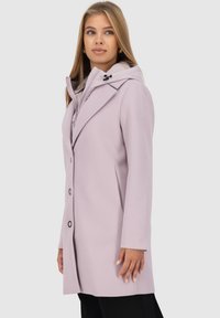 Cappotto viola chiaro con design aderente, revers strutturati, chiusura con bottoni e cappuccio. Texture liscia con una silhouette pulita.