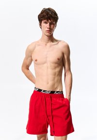 Pantaloni da bagno rossi realizzati in tessuto leggero con una fascia elastica nera in vita con logo, progettati con tasche laterali e un cordoncino regolabile.