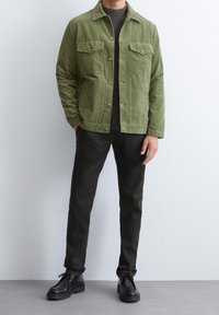 Vihreä corduroy-takki, jossa on kaksi rintataskua, yhdistettynä tumman neulospaidankin ja slim fit mustiin housuihin. Mustat nauhapedearit viimeistelevät asun.