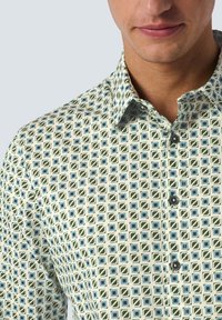 Kraagshirt met een geometrisch patroon in groen, blauw en crème. Gemaakt van een lichte stof met zwarte knopen.