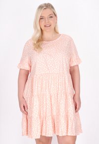 Světle broskvová, šaty ke kolenům vyrobené z měkkého materiálu. Mají bílé puntíky, krátké volánkové rukávy a sukni s vrstveným designem.