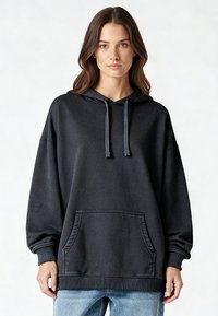 Fekete kapucnis pulóver laza szabással, húzózsinórokkal, első zsebbel, bordázott aljjal és mandzsettákkal. Puha tapintású, laza, hétköznapi stílus.