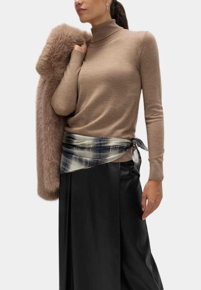 Beżowy sweter z długim rękawem i stójką w połączeniu z czarną plisowaną spódnicą; miękki brązowy szal z sztucznego futra zarzucony na ramię, akcentowany pasiastym szalikiem.