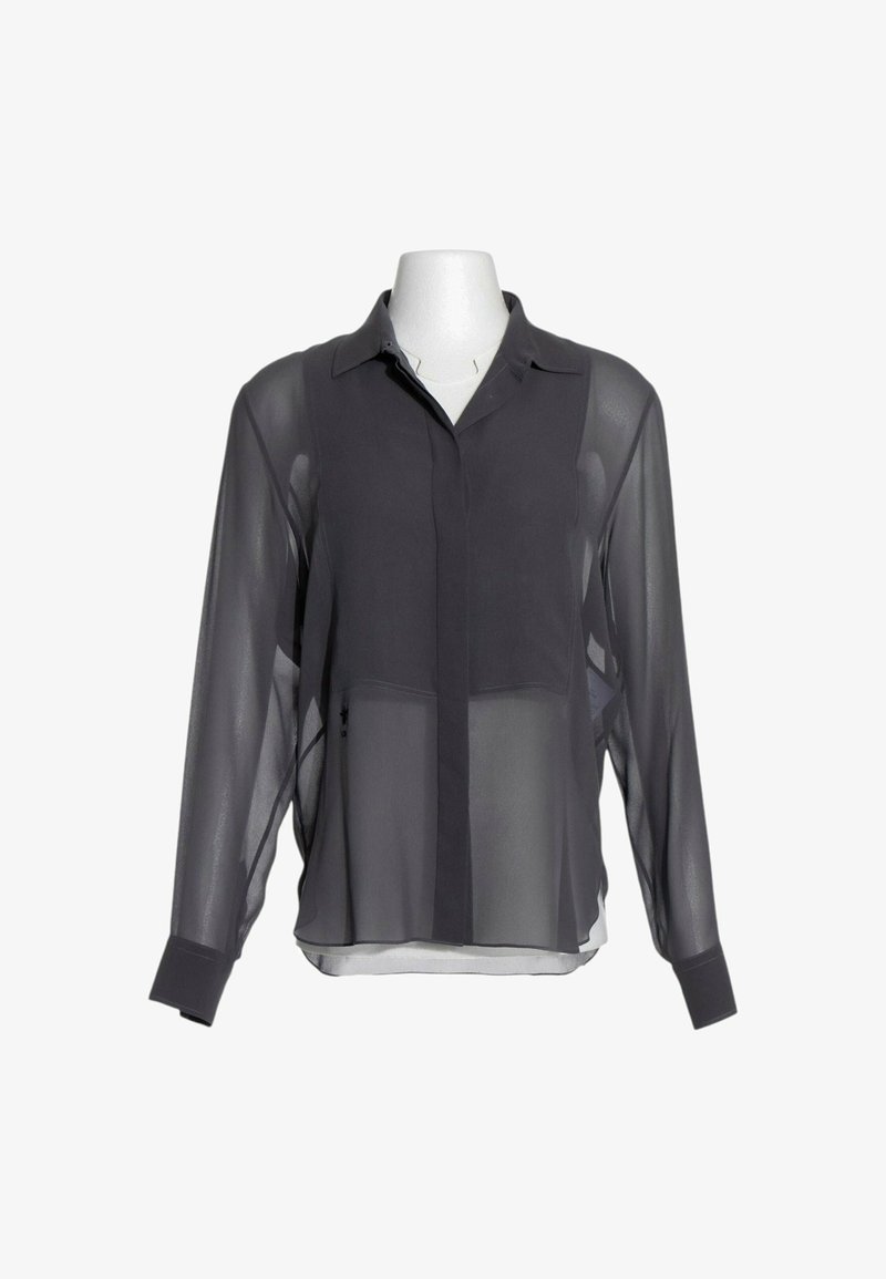 Blouse noire transparente à manches longues avec panneau poitrine uni, poignets boutonnés et col classique, présentée sur un buste de mannequin blanc.