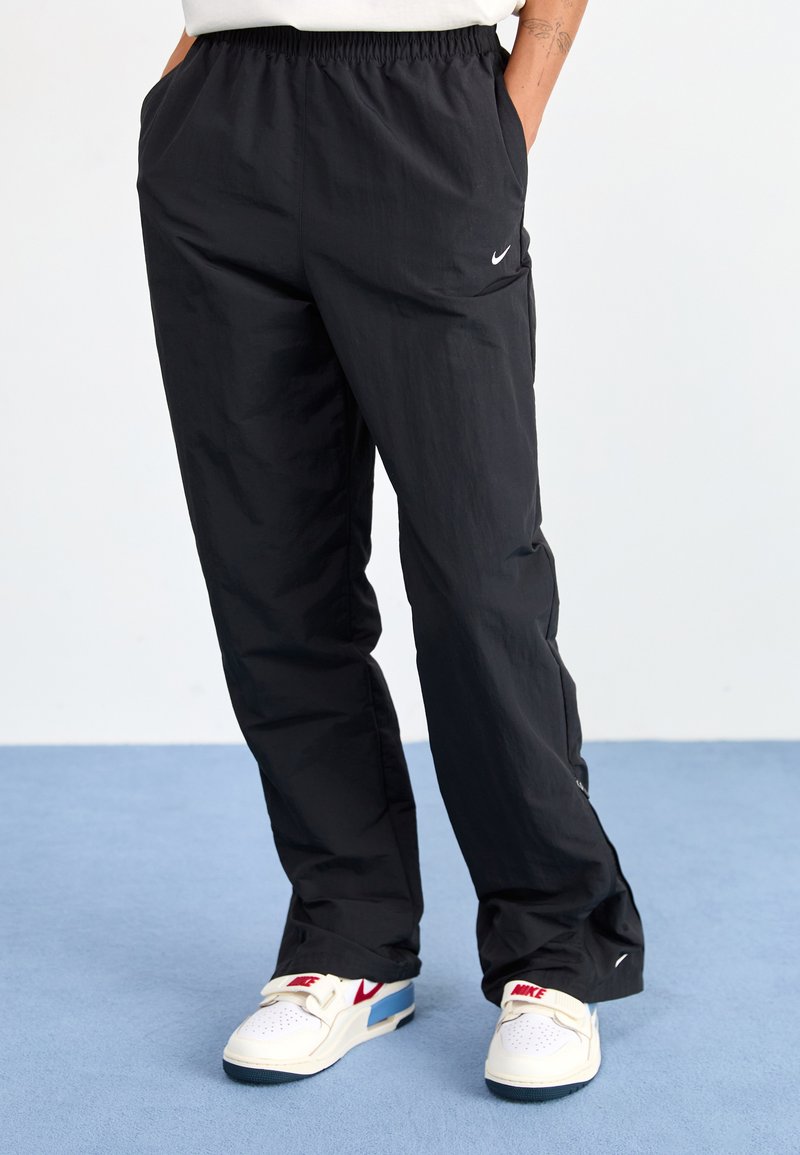 Schwarze Nylon-Tracking-Hosen mit elastischem Bund, seitlichen Taschen und einem kleinen weißen Nike-Logo am linken Oberschenkel.
