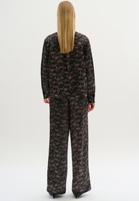 Svart- och brunt mönstrad tvådelad outfit som har en långärmad skjorta och vida byxor, tillverkad av ett mjukt och slätt tyg.